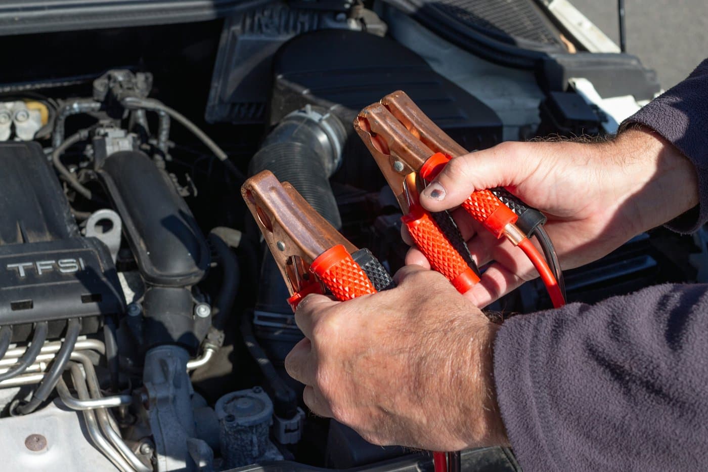 Technician holding jumper cable clamps over an open engine bay